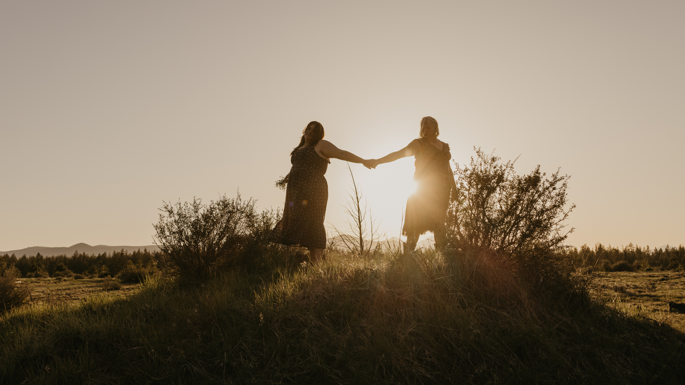 Two people holding hands in a field with the sun setting behind them